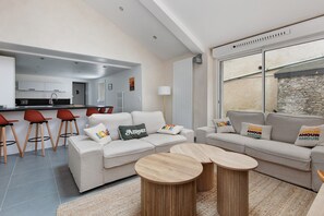 Een moderne woonkamer met een bank, twee ronde houten bijzettafels en rode barstoelen.