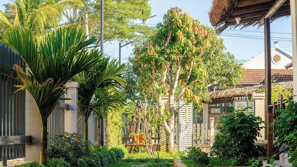 Un sentier de jardin mène à un bâtiment doté d’un toit traditionnel recouvert de tuiles et d’une structure de toit en chaume.