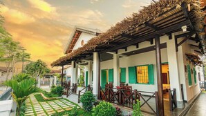 Un bâtiment traditionnel doté d’un patio couvert, d’un espace extérieur aménagé pour s’asseoir et d’un sentier qui traverse le jardin.