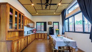 Une cuisine spacieuse avec des meubles en bois, une table à manger pour quatre personnes et de grandes fenêtres donnant sur l’extérieur.