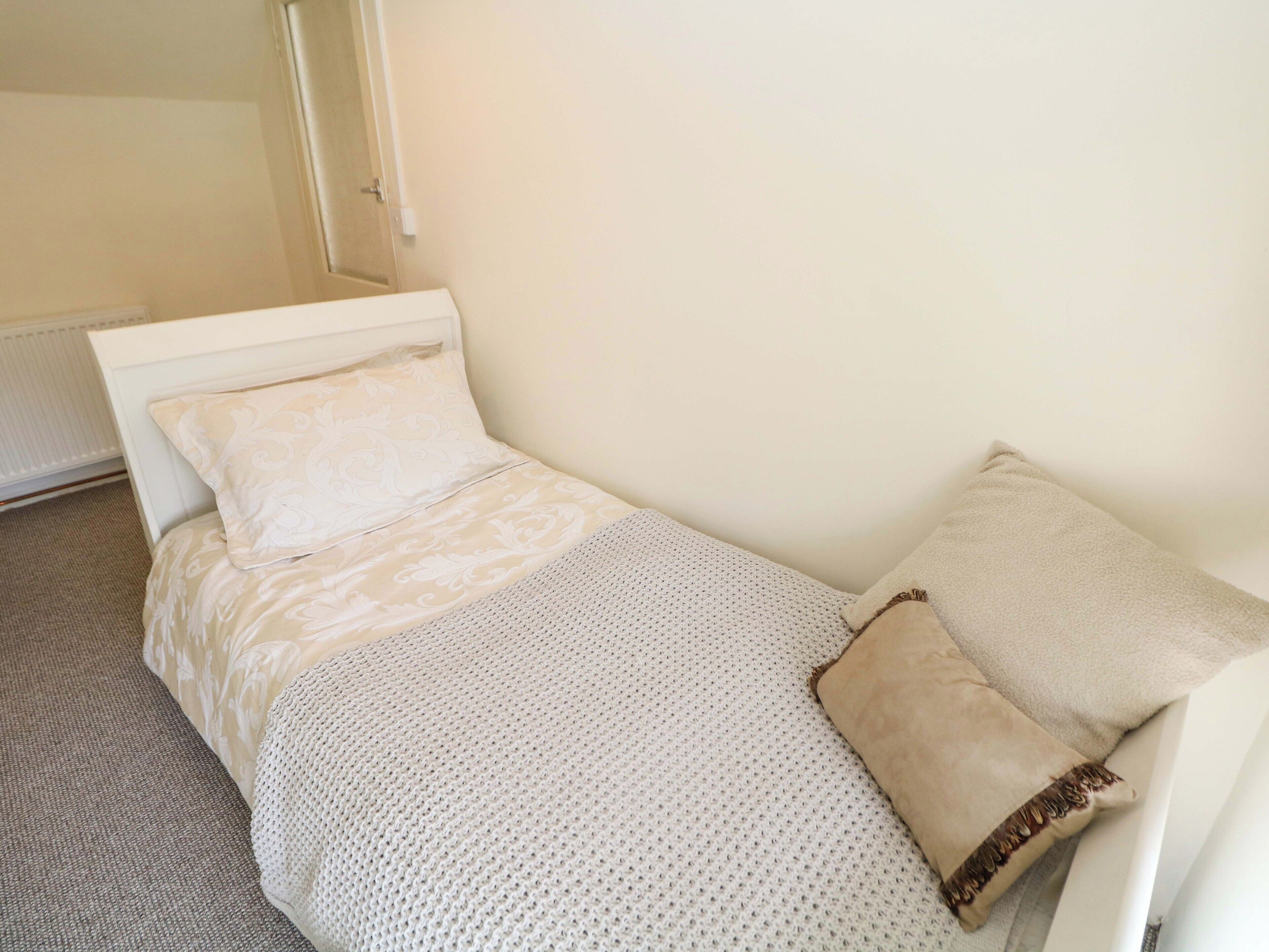 Une petite chambre avec un lit simple, une tête de lit blanche, une couvre-lit à motifs et deux oreillers.