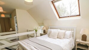 Un dormitorio con una cama litera, una mesita de noche con lámpara, una ventana con vistas a árboles y una planta junto a la cama.