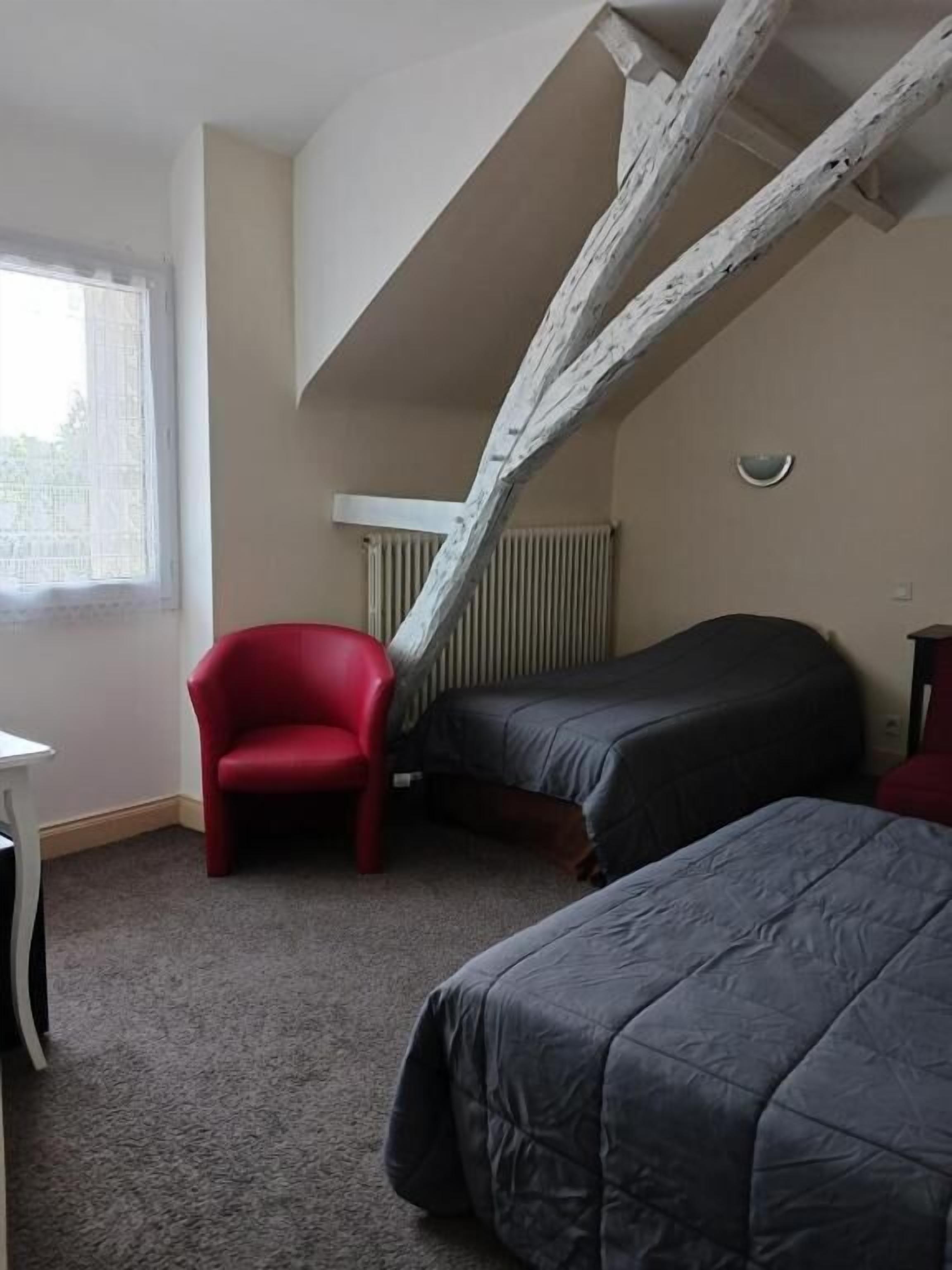 Una habitación con dos camas, una silla roja y una mesa blanca.