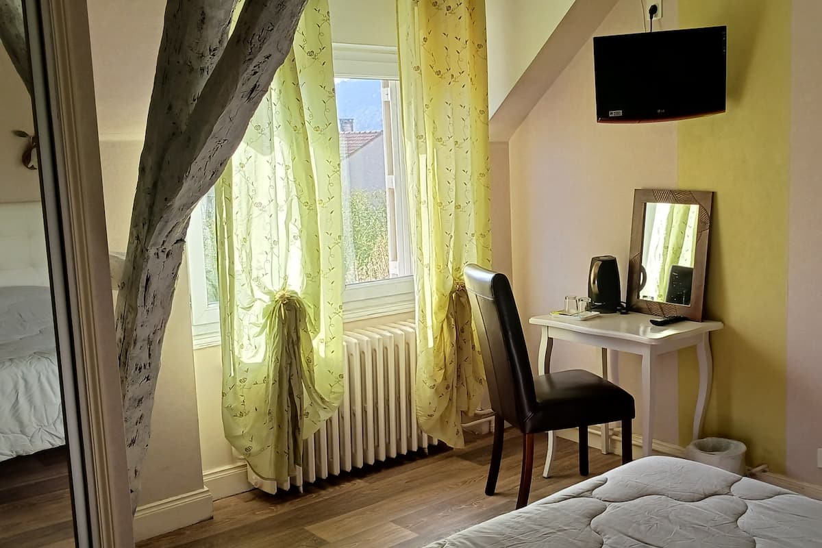 A bedroom with a bed, a desk, a chair, a radiator, and a TV mounted on the wall.