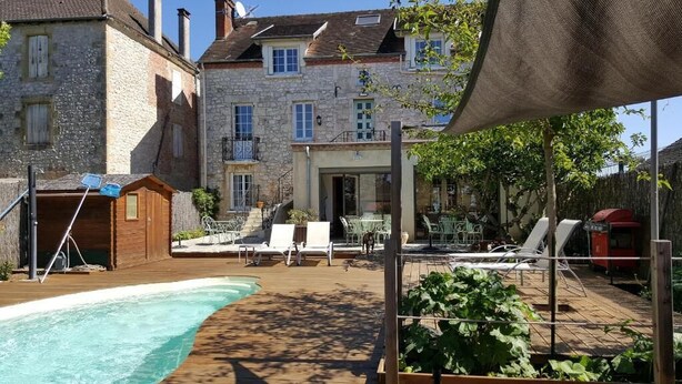 Un espace piscine doté de chaises longues et d’un barbecue, le tout entouré de bâtiments en pierre.