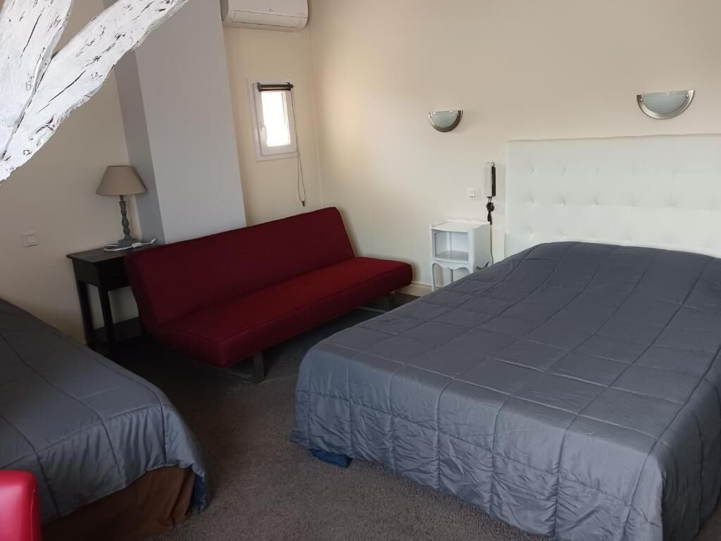 Una camera da letto con due letti, un divano rosso, un tavolino con una lampada e una finestra.