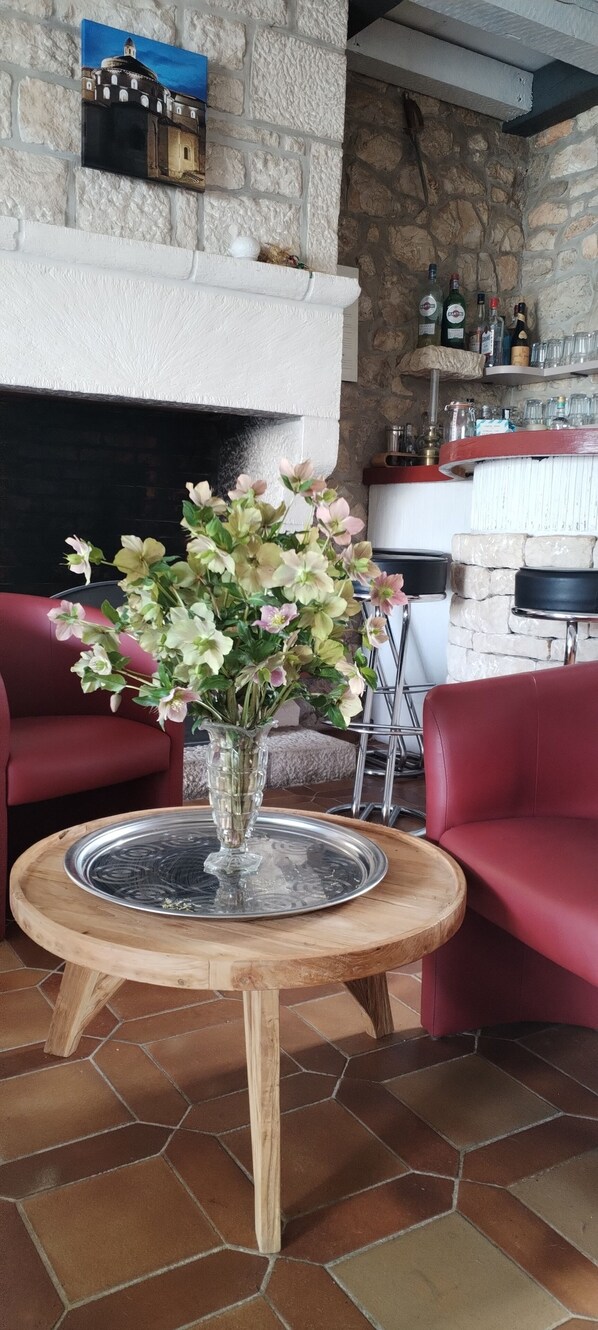 A room with a stone fireplace, a round wooden table with a glass top, and two red chairs. - hôtel du Puy d Alon (Souillac)