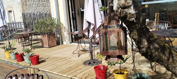 Un patio al aire libre con mesas y sillas de madera, plantas en macetas y un farol decorativo.