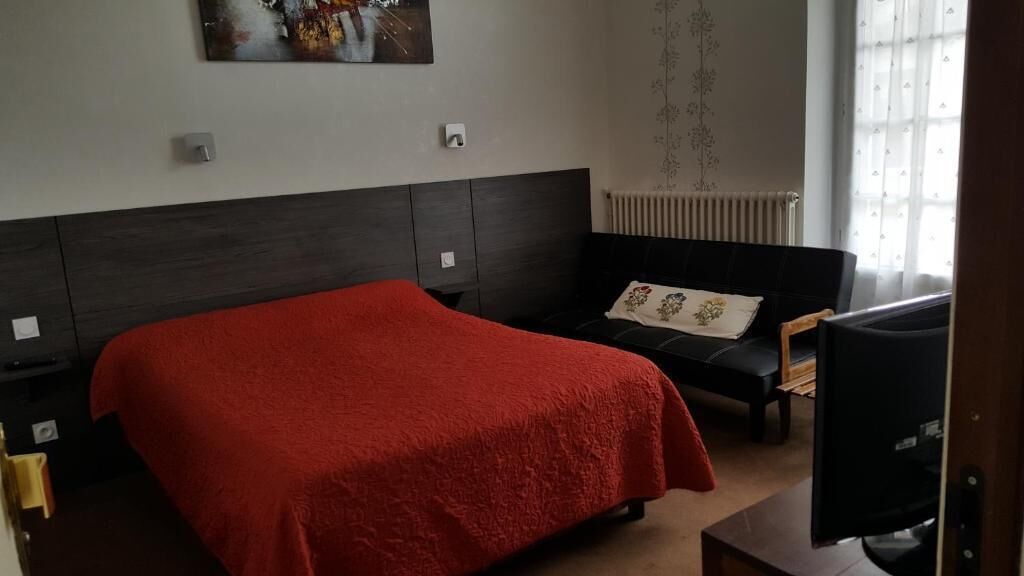 Un dormitorio con una cama grande, un sofá negro, un televisor y un radiador.