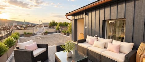 A rooftop terrace with wicker furniture, a hanging chair, and potted plants.