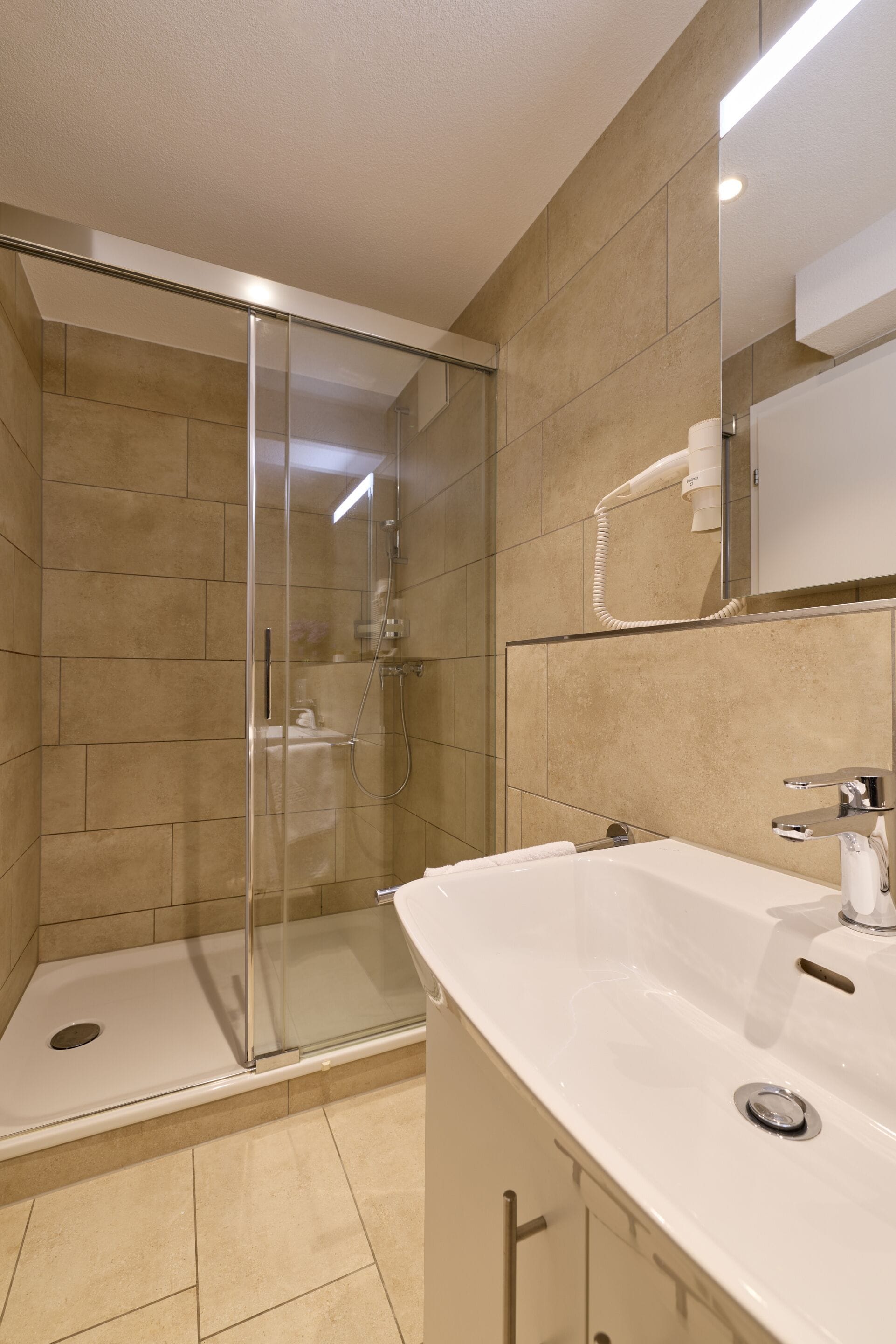 A modern bathroom with a glass-enclosed shower, a white sink, and a mirror above the sink.