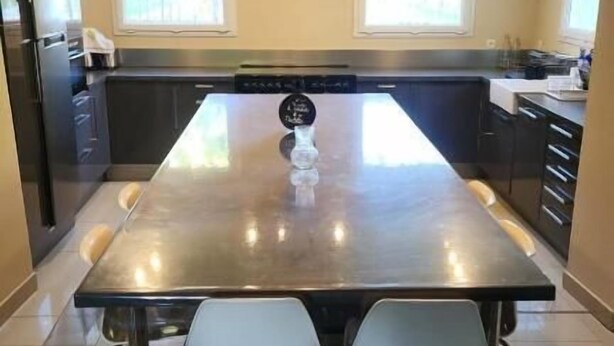A modern kitchen with a large island, two bar stools, and a hanging light fixture. - Chambres Domaine de Saint Marc (Saint-Médard)