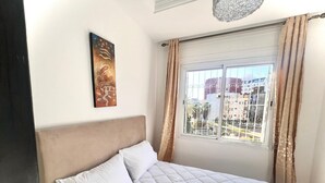 Ein Schlafzimmer mit Bett, Vorhängen an einem Fenster und einem Gemälde an der Wand.