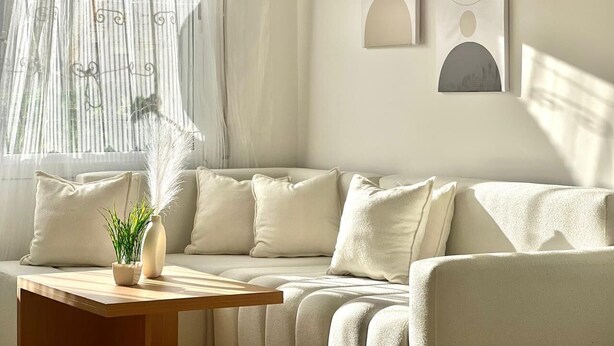 Ein modernes Wohnzimmer mit einem beigefarbenen Sofa, einem Holztisch und einer Topfpflanze.