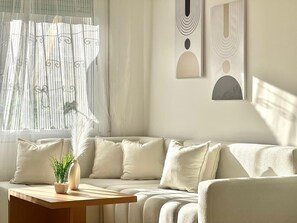 Uma sala de estar moderna com um sofá bege, uma mesa de centro de madeira e um vaso com planta.