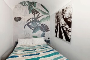 Een slaapkamer met een bed, een muurschildering van tropische bladeren en een schilderij van bomen.