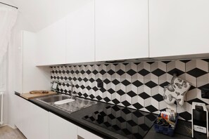 Een keuken met een zwart-wit betegelde spatwand, een roestvrijstalen spoelbak en een aanrecht met een snijplank en een blauwe mand.