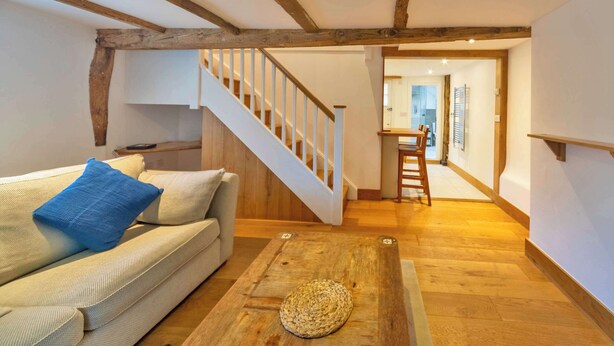Een gezellige woonkamer met een houten trap, een bank met kussens en een geweven vloermat.
