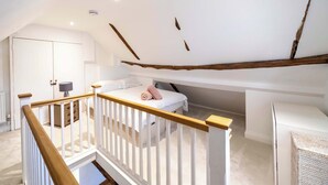 Een slaapkamer met een schuine kap, een houten trap, een bed met kussens, een nachtkastje en een kledingkast.