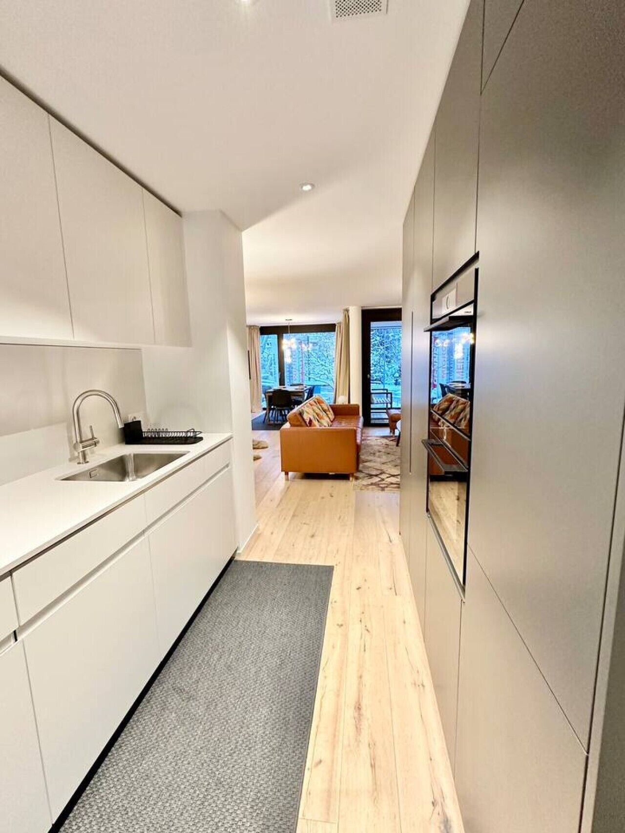A modern kitchen with a built-in oven, a sink, and a dining area with a sofa and table.