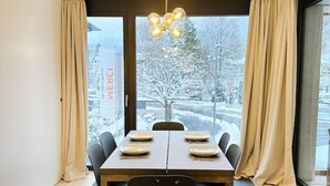 En matplats med ett bord för fyra personer, en modern kristallkrona och stora fönster med gardiner.