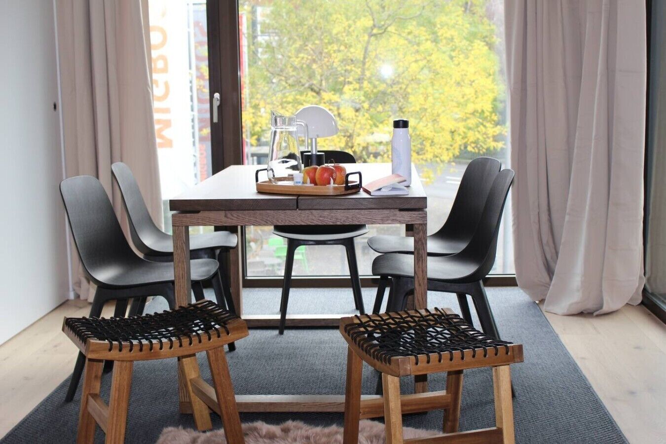 Een eetruimte met een houten tafel, vier stoelen, een kleedje en een raam met gordijnen.