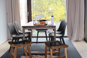 En spiseplads med et træbord, fire stole, en mindre måtte og et vindue med gardiner.