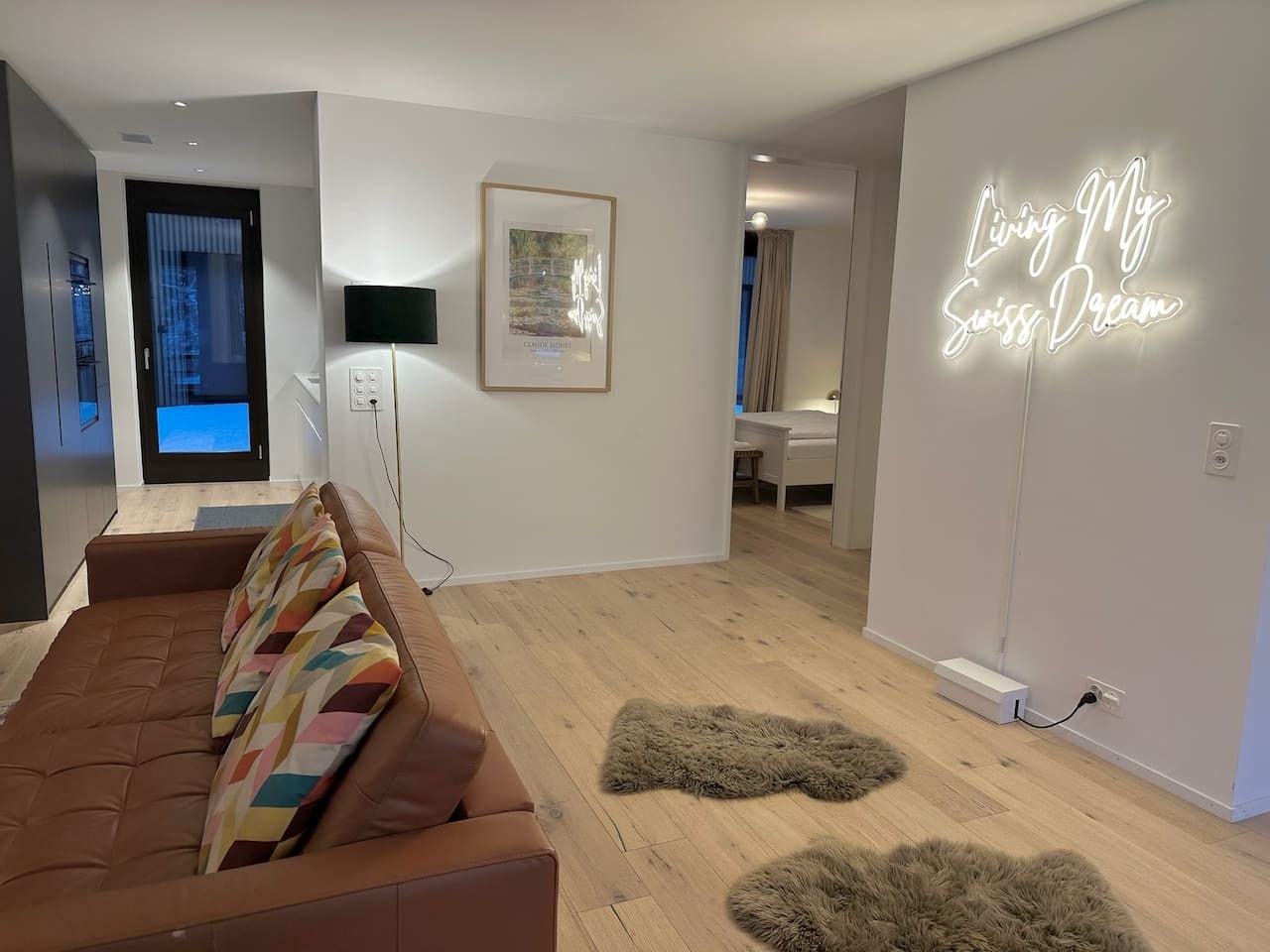 Ett modernt vardagsrum med en brun soffa, en inramad tavla på väggen och en neonskylt med texten ”Jag lever min schweiziska dröm”.