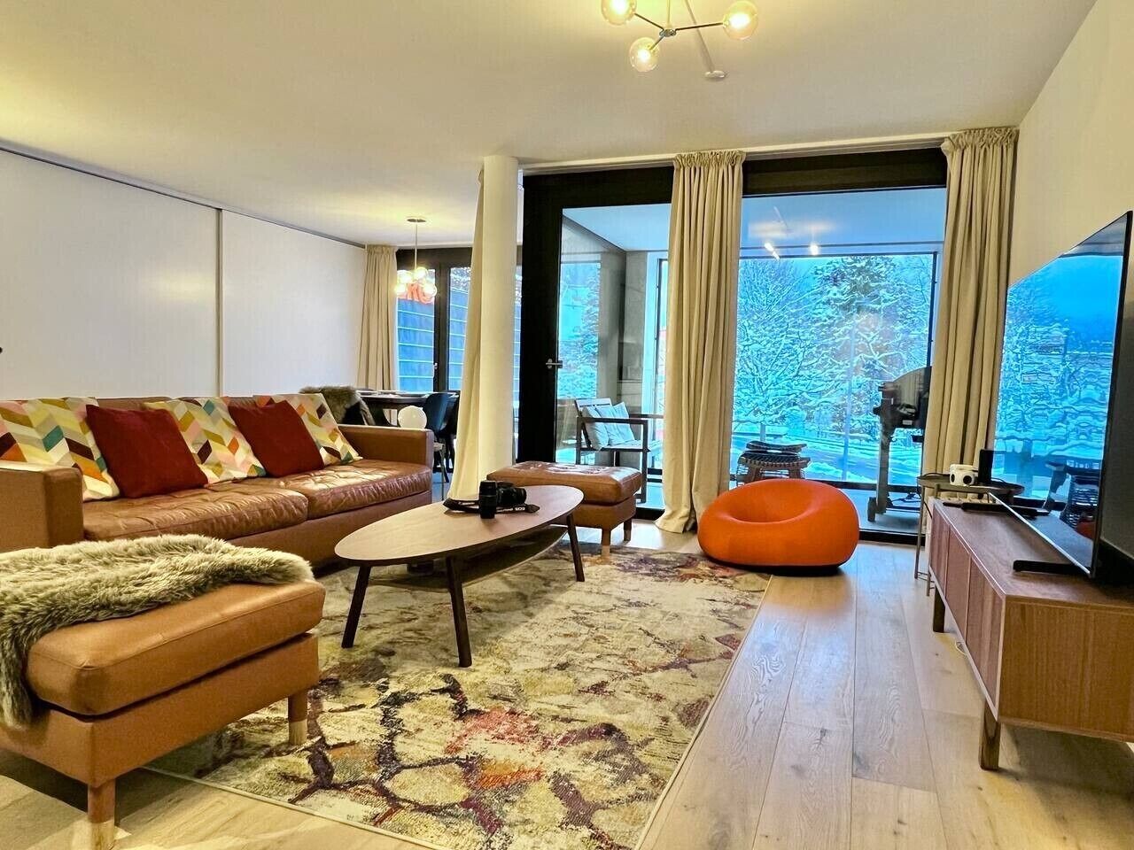 Een moderne woonkamer met een leren bank, een salontafel en een oranje relaxfauteuil.