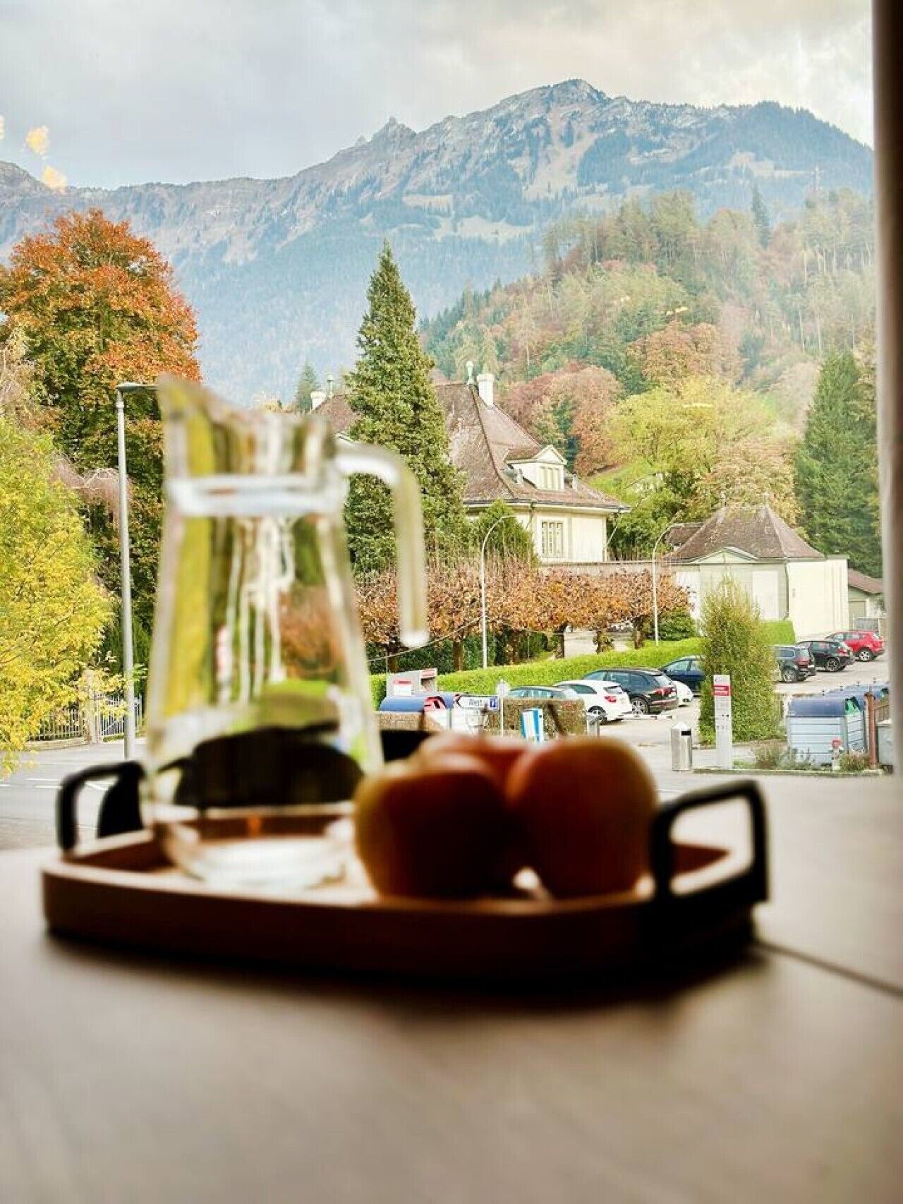 A view of a mountain landscape through a window, with a pitcher and glasses on a table in the foreground.
