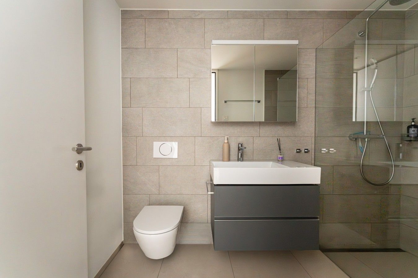 A modern bathroom with a toilet, a sink with a mirror above, and a shower area.