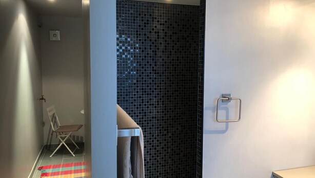 Ein modernes Badezimmer mit gefliesten Duschwänden, einem Handtuchhalter und einer kleinen Sitzecke mit farbenfrohem Teppich.