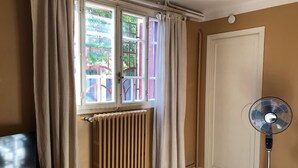 Ein Zimmer mit Heizkörper, Standventilator und einem fenster mit Vorhängen.