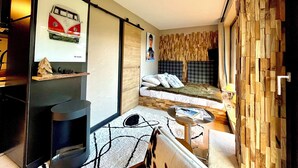 Een knus slaapkamer met een bed, een klein tafeltje, een stoel, een houten wandpaneel en een lijst met een afbeelding.