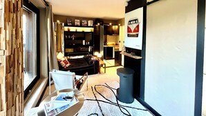Een moderne woonkamer met een bank, salontafel en een open haard. Achtergrond heeft een boekenkast en een televisie.
