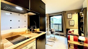 Een moderne keuken met een inbouwfornuis, een spoelbak en een koffiezetapparaat. Er is een eethoek met een tafel en stoelen, en een uitzicht op het buitengebied door een groot raam.