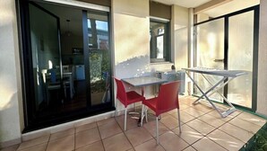 Un balcó amb una taula i dues cadires, una porta corredissa de vidre i vistes cap a l'exterior.