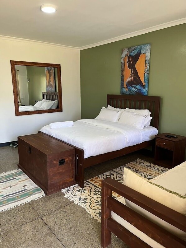 A bedroom with a wooden bed, a nightstand, a mirror, and a painting on the wall. - Riverside Villas Nanyuki (Nanyuki)