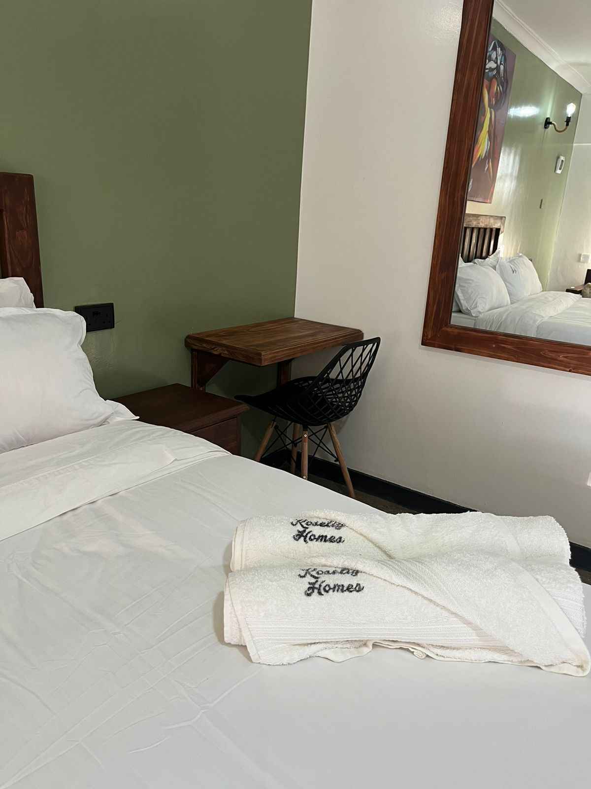 Une chambre d’hôtel avec un lit, une table en bois, une chaise et un miroir.