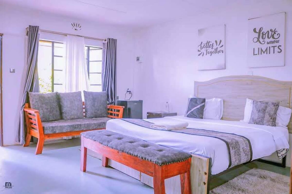 Un dormitorio con cama, una banca, un sofá y dos ventanas con cortinas.
