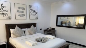 A neatly made bed with pillows, a bedside table with a lamp, and a mirror on the wall. - Riverside Villas Nanyuki (Nanyuki)