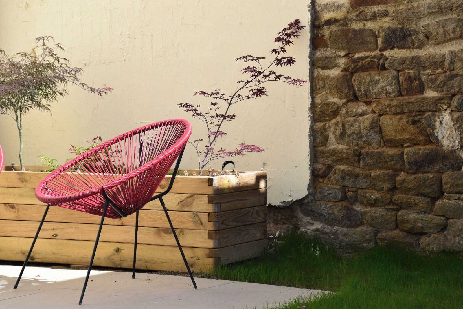 A pink chair, wooden planter, and a stone wall.