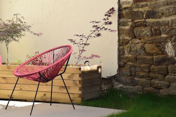 A pink chair, wooden planter, and a stone wall.