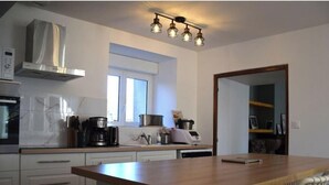 Una cocina moderna con campana de acero inoxidable, cafetera y microondas. Hay una ventana sobre el fregadero y una puerta que da a otra habitación.