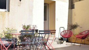 Un patio al aire libre con mesa y sillas, un pequeño jardín y una puerta que da al interior.