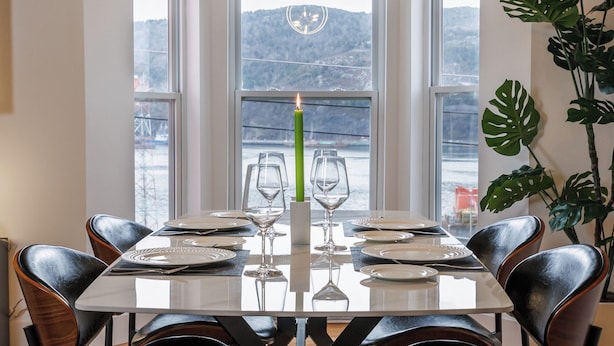 A dining area with a large table set for six, surrounded by leather chairs, with a view of a mountainous landscape through large windows. - Lime Suite at Jellybean House (St. John's)