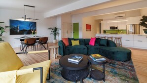 A modern living room with a green sectional sofa, a yellow armchair, and a dining area with a table and chairs. - Lime Suite at Jellybean House (St. John's)