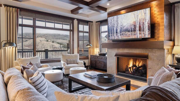 Una sala de estar amplia con chimenea, ventanas grandes y un televisor montado en la pared.