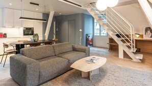 A modern living room with a grey sofa, a wooden coffee table, and a staircase leading to an upper level. - Luxury & Design duplex - 5 min from Louvre Museum - 6 guests (Paris)