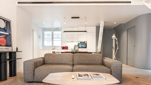 A modern living room with a sofa, a coffee table, and a kitchen in the background. - Luxury & Design duplex - 5 min from Louvre Museum - 6 guests (Paris)